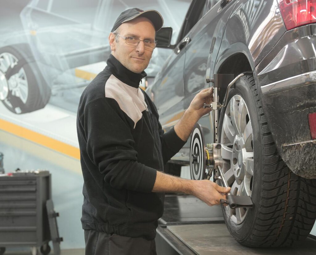 Mechanic performing wheel alignment on a car in a professional garage setting.